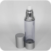 A cylindrical, transparent spray bottle with a silver cap placed beside it. The bottle's spray nozzle and collar are metallic and glossy. The background is plain and light-colored.