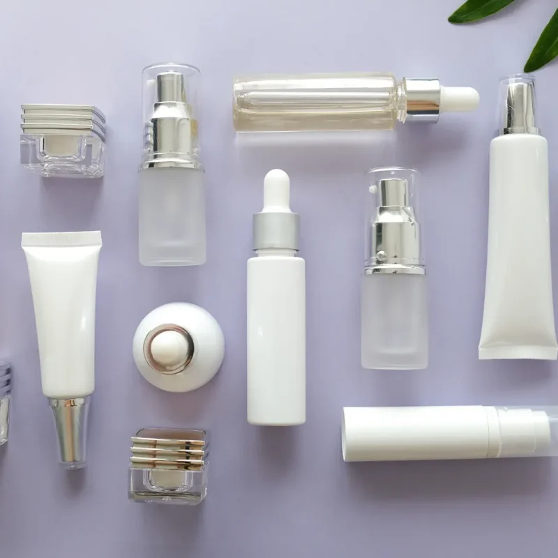 A variety of skincare and cosmetic bottles and tubes in white and clear designs are laid out against a light purple background. The arrangement also includes a few green leaves on the sides, adding a natural touch to the minimalistic composition.