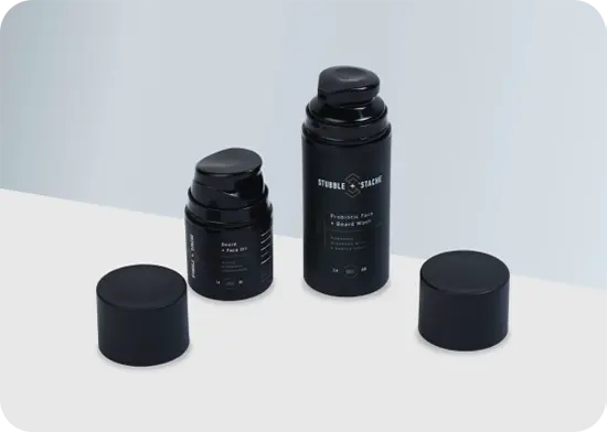 Two black pump bottles with black caps on a white and light gray background. Caps are off and placed beside each bottle.