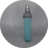 A tall, rectangular pump bottle with a blue liquid inside and a reflective silver cap. The bottle stands against a plain gray background. The cap has a clear, cube-shaped cover placed beside the bottle.
