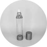 A cylindrical, clear airless pump bottle with a silver cap sits on a white surface. The cap is removed and placed next to the bottle, revealing the pump mechanism. The bottle is empty, and the image is in grayscale.