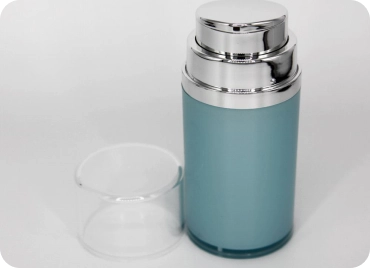 A cylindrical, blue cosmetic container with a shiny silver cap is displayed against a white background. To the left of the container, there is a clear plastic lid placed beside it.